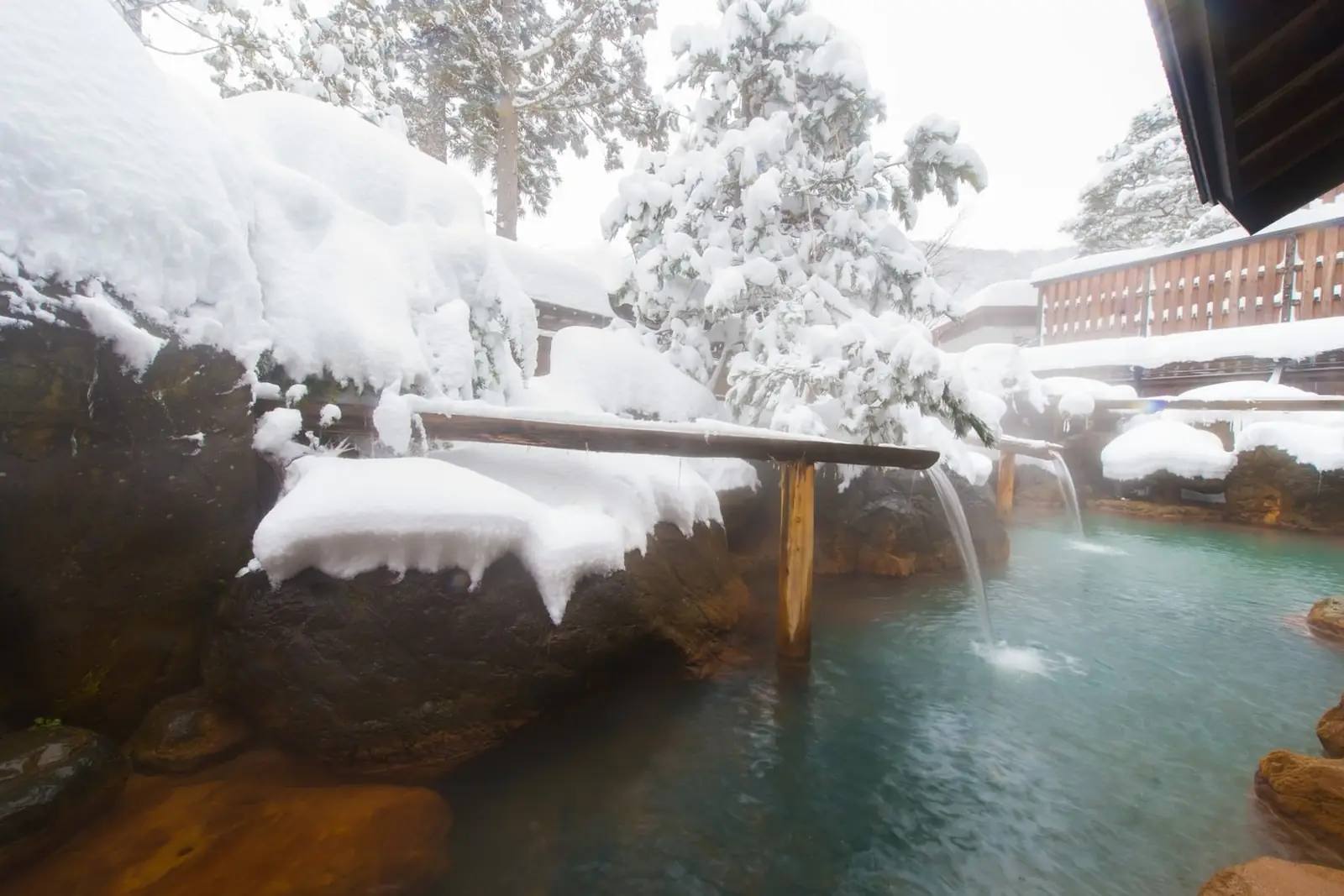 Verschneites offenes Onsen-Bad im Wald, dampfendes Thermalwasser, niemand zu sehen