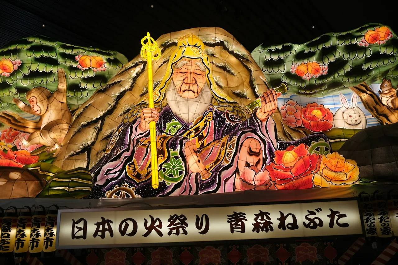 Riesiger, von innen beleuchteter Figuren-Wagen beim Nebuta Matsuri in Aomori — ein leuchtender Kriegergott aus bemaltem Washi-Papier vor dem Nachthimmel