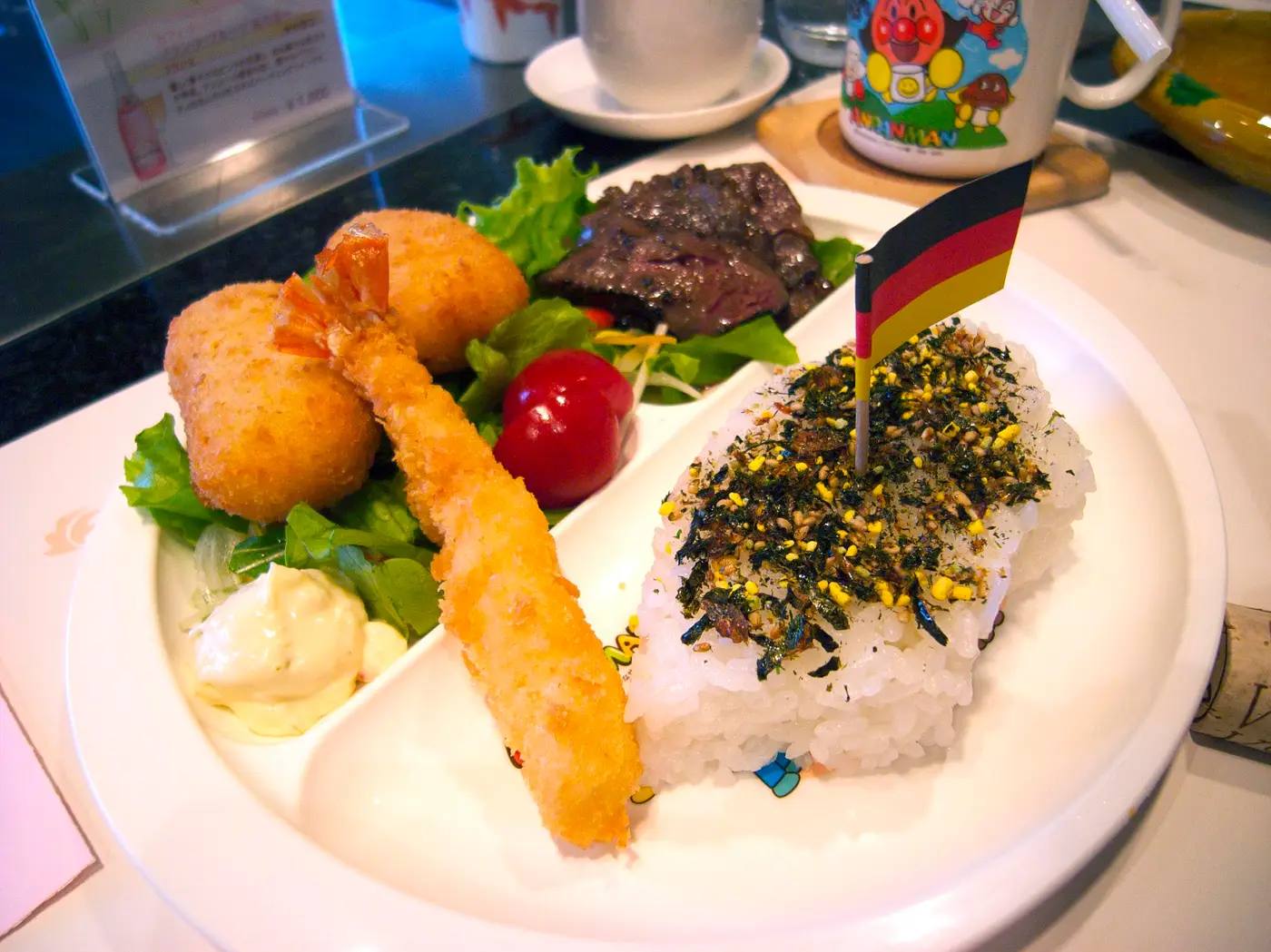 Ein Okosama-Lunch, der japanische Kinderteller, mit Reis, frittierten Garnelen, Croquettes und einem kleinen Fähnchen in Schwarz-Rot-Gold