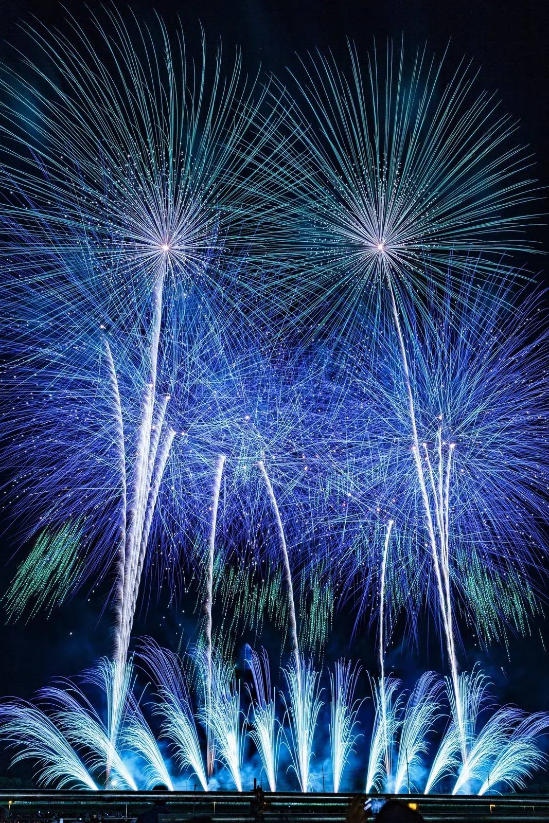 Blaues Starmine-Feuerwerk beim nationalen Feuerwerkswettbewerb von Ōmagari in Akita — fächerförmige Lichtfontänen und große runde Leuchtblüten am Nachthimmel