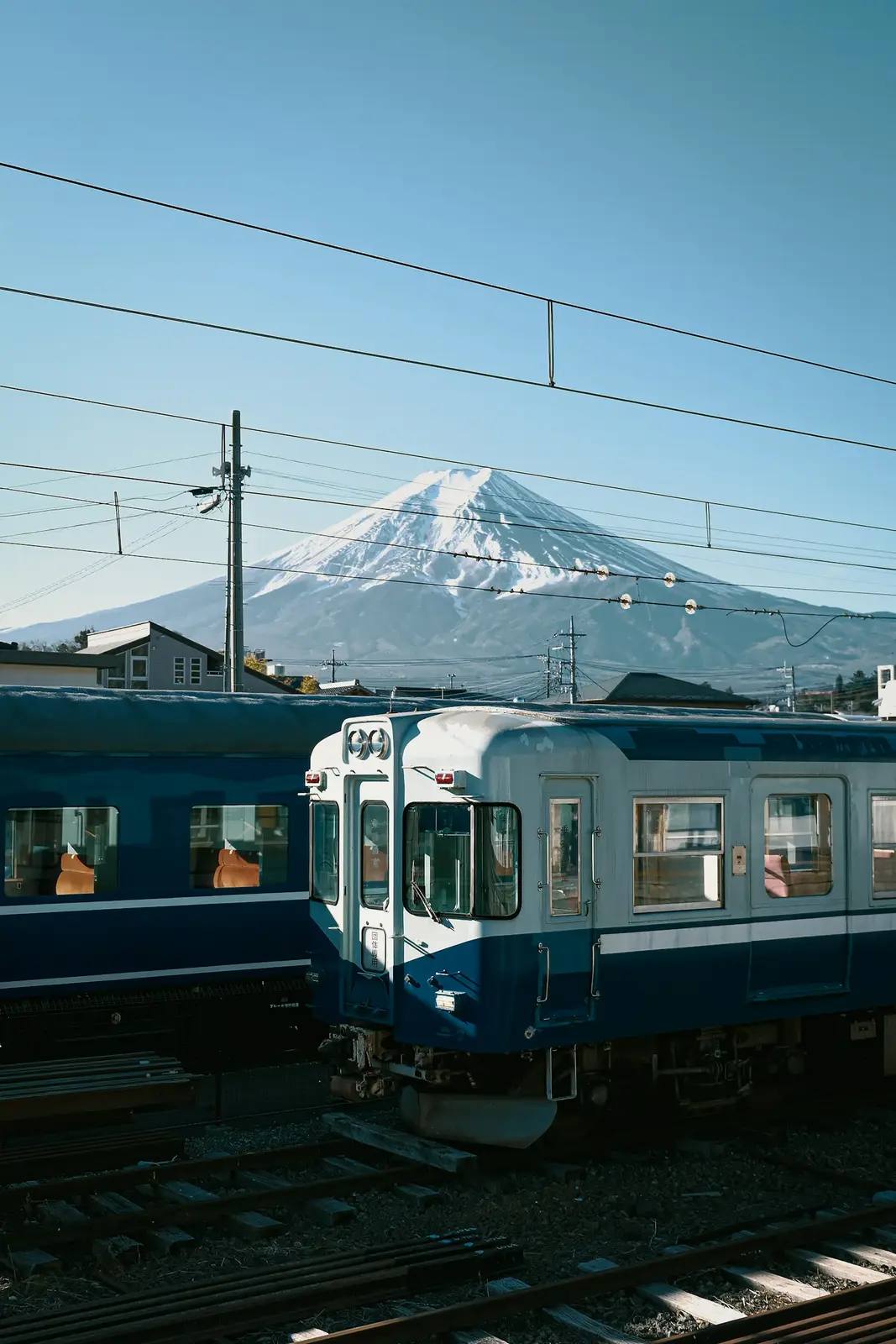 Ein blau-weißer Zug steht vor dem schneebedeckten Berg Fuji unter klarem Himmel – sinnbildlich für die Reise durch Japan und die Wahl zwischen Pauschalreise und Individualreise