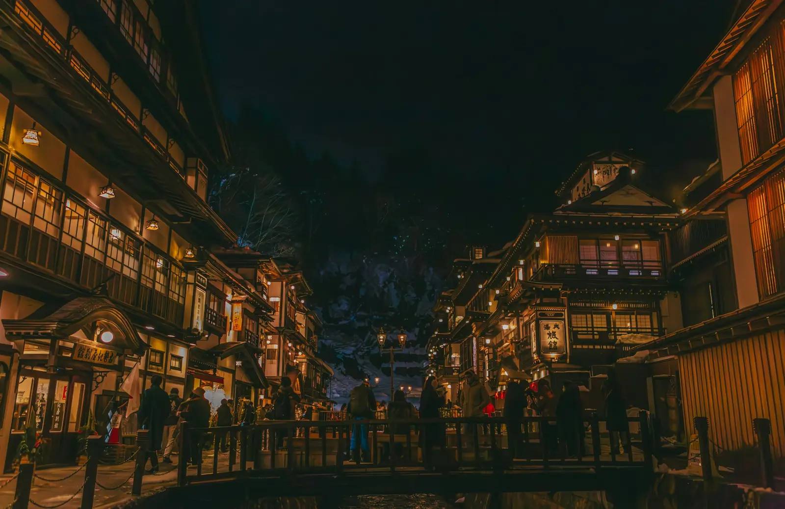 Die historische Gasse von Ginzan Onsen bei Nacht, gesäumt von beleuchteten traditionellen Ryokan