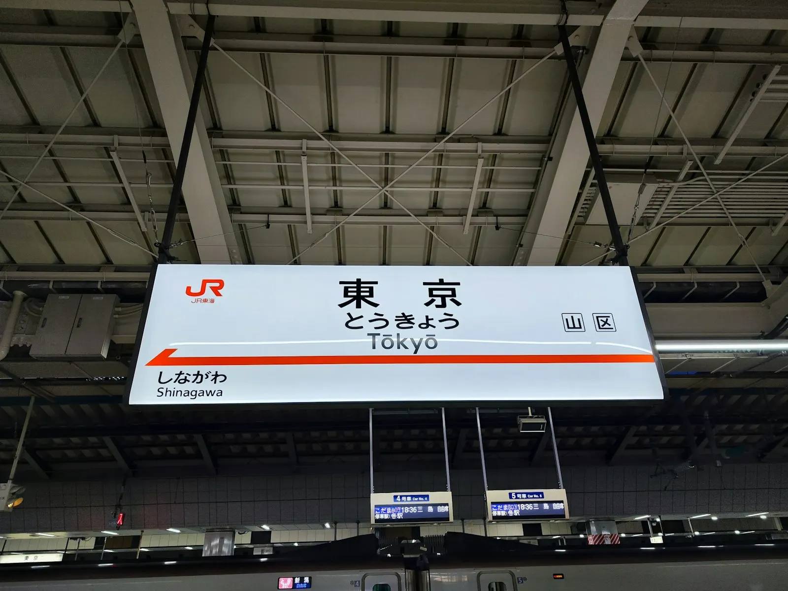 Beleuchtetes Stationsschild „東京 – Tōkyō“ am Shinkansen-Bahnsteig, darunter zwei kleine Anzeigen mit den Wagennummern 4 und 5.