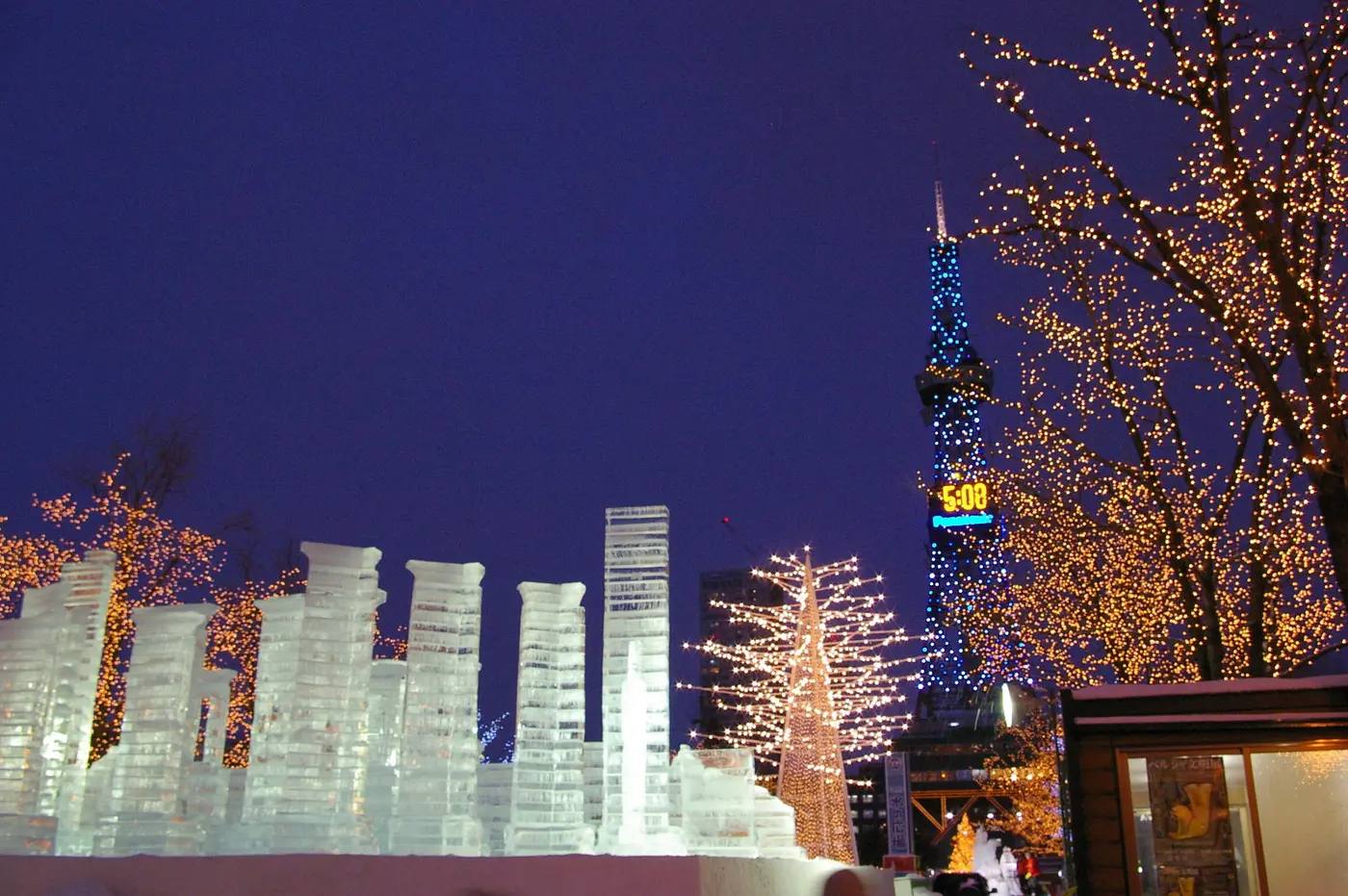 Beleuchtete Eisskulpturen beim Sapporo Schneefestival im Odori-Park bei Nacht, im Hintergrund der blau angestrahlte Sapporo-Fernsehturm