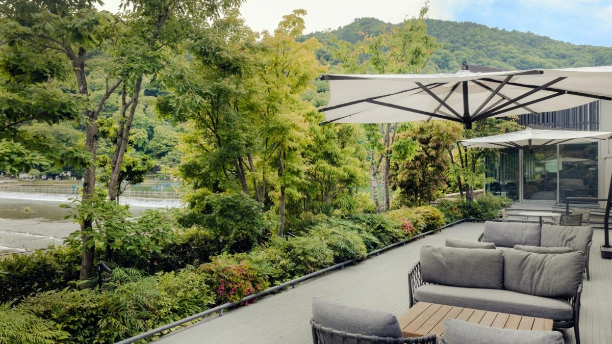 Sonnige Terrasse des Riverside Café MUNI in Arashiyama, mit Fluss und grünen Berghängen