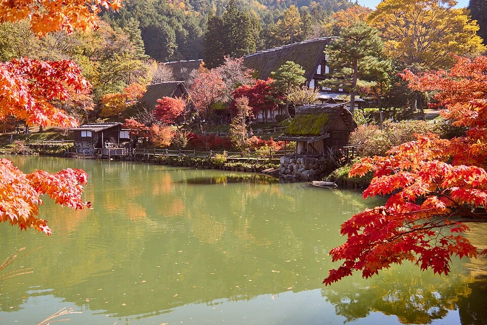 Traditionelle Häuser am Teich im Hida Folk Village in Takayama, umgeben von Herbstlaub